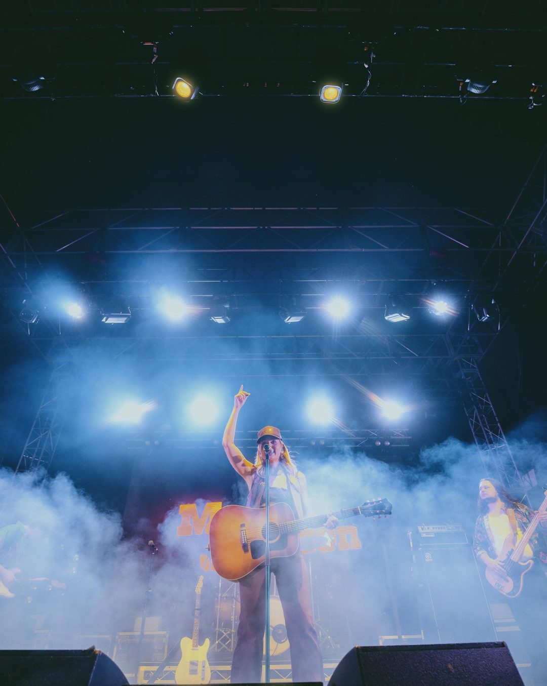 Max Jackson on stage at Country Fest QLD, arm raised, under white beams and haze