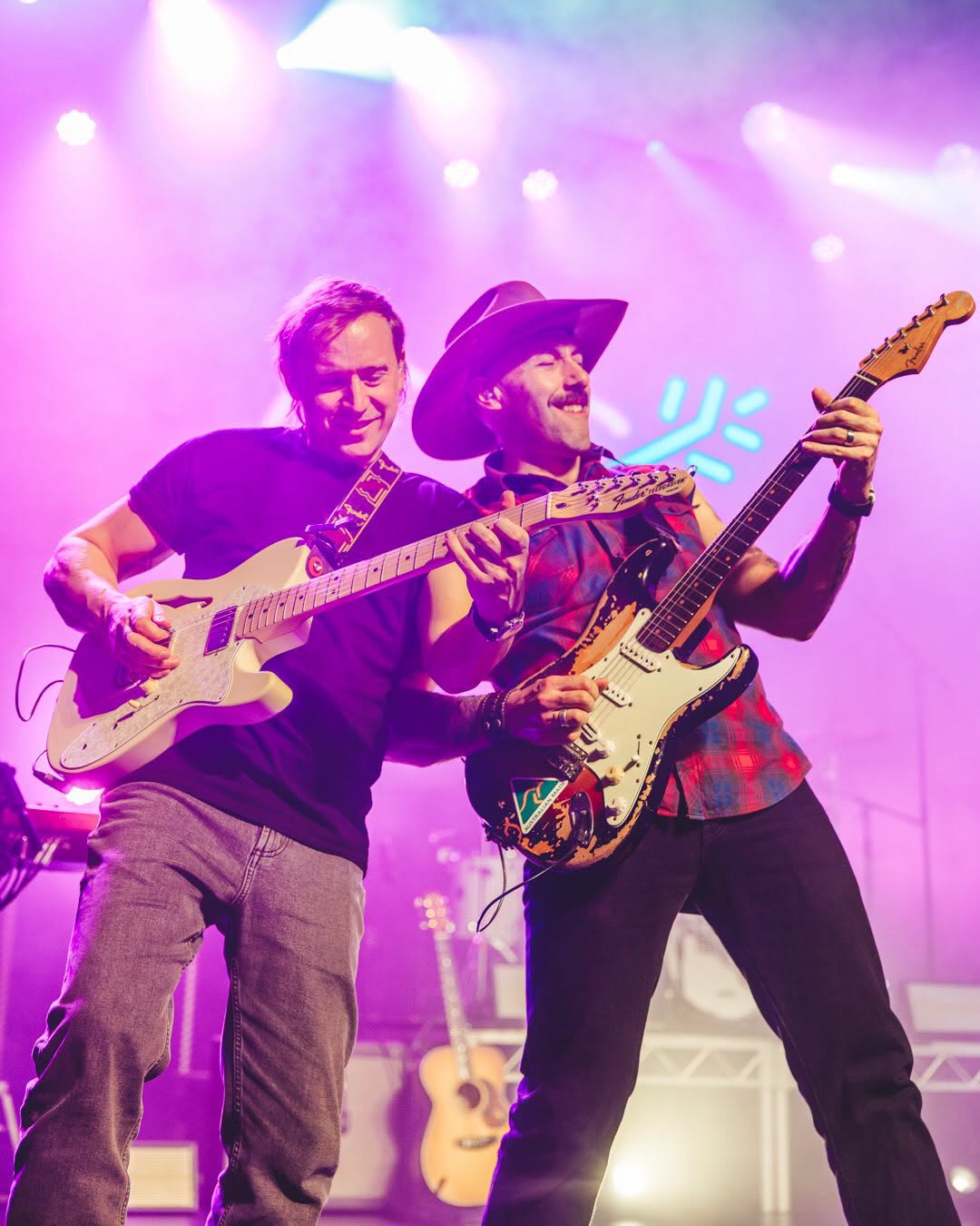Two Wolfe Brothers guitarists playing side by side under pink stage light